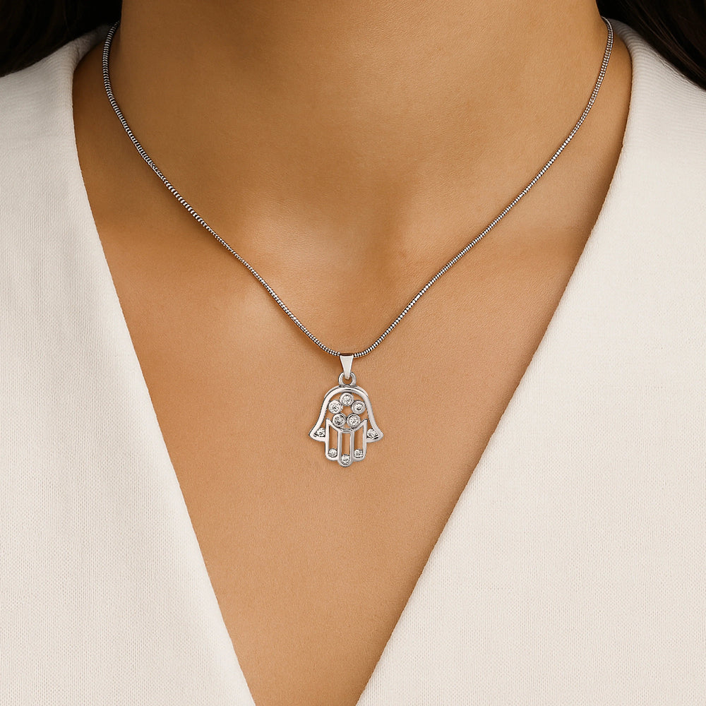 Silver Hamsa necklace with clear stones on a model wearing a white top.