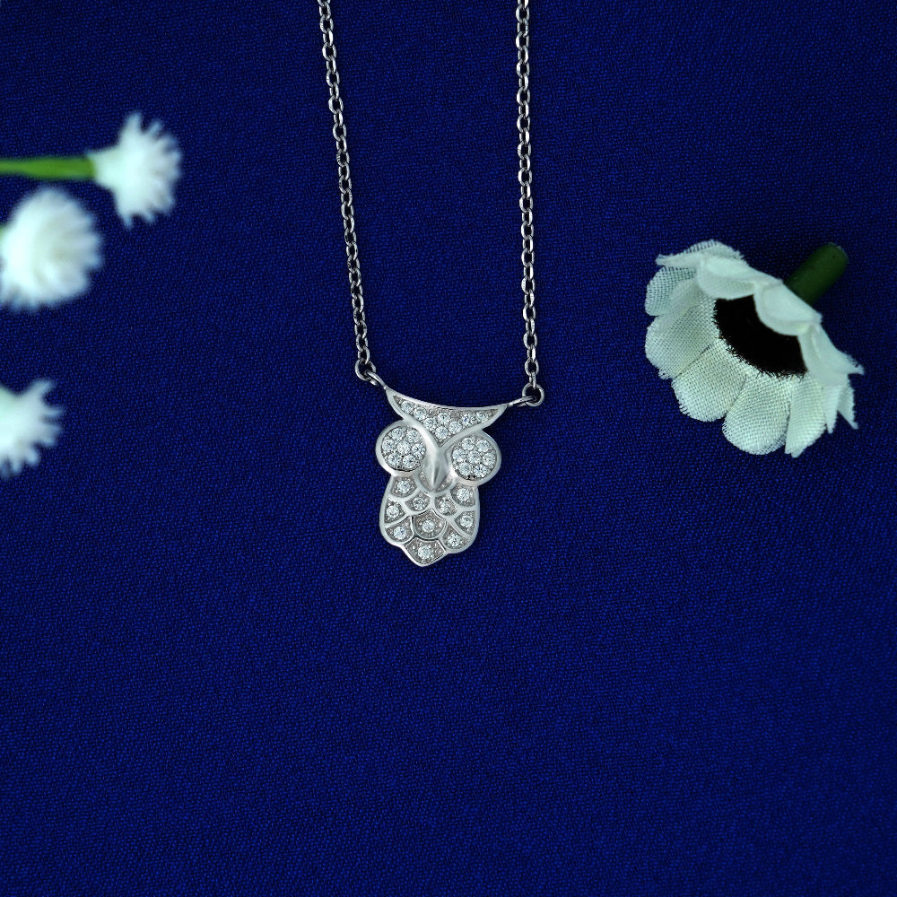 Silver necklace with a floral pendant on a blue background with white flowers.