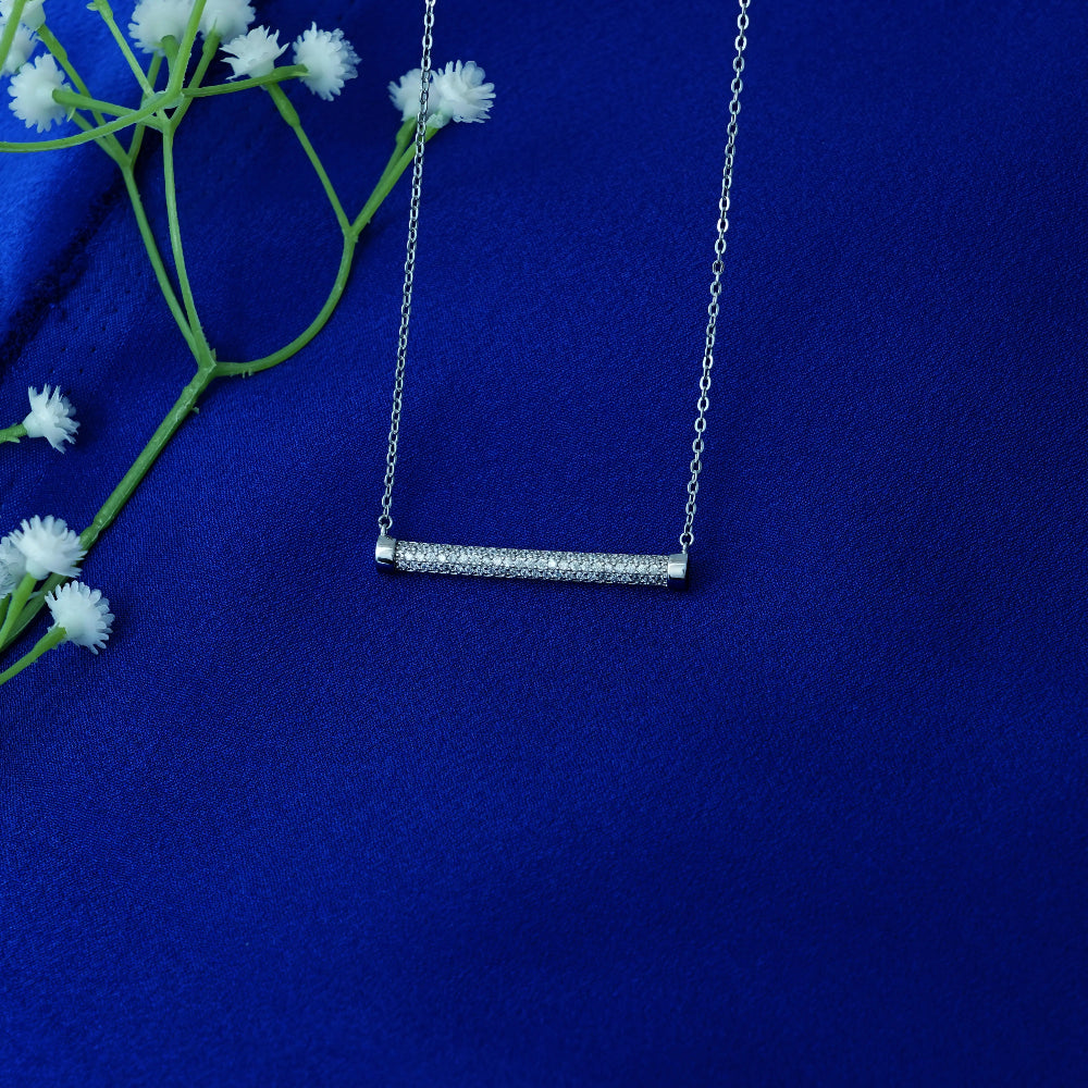 Silver necklace with a bar pendant on a blue background with white flowers